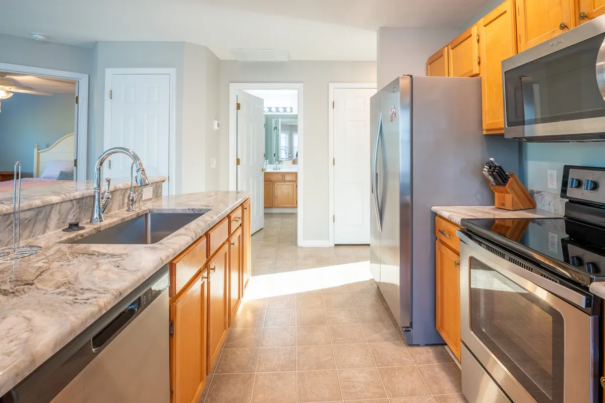 This image presents a welcoming kitchen with a prominently featured island, granite countertop, and modern stainless steel appliances. The island is equipped with seating, suggesting a space for casual meals or friendly conversation while cooking. The setting is bright and inviting, with ample counter space and a layout ideal for both meal prep and entertaining.
