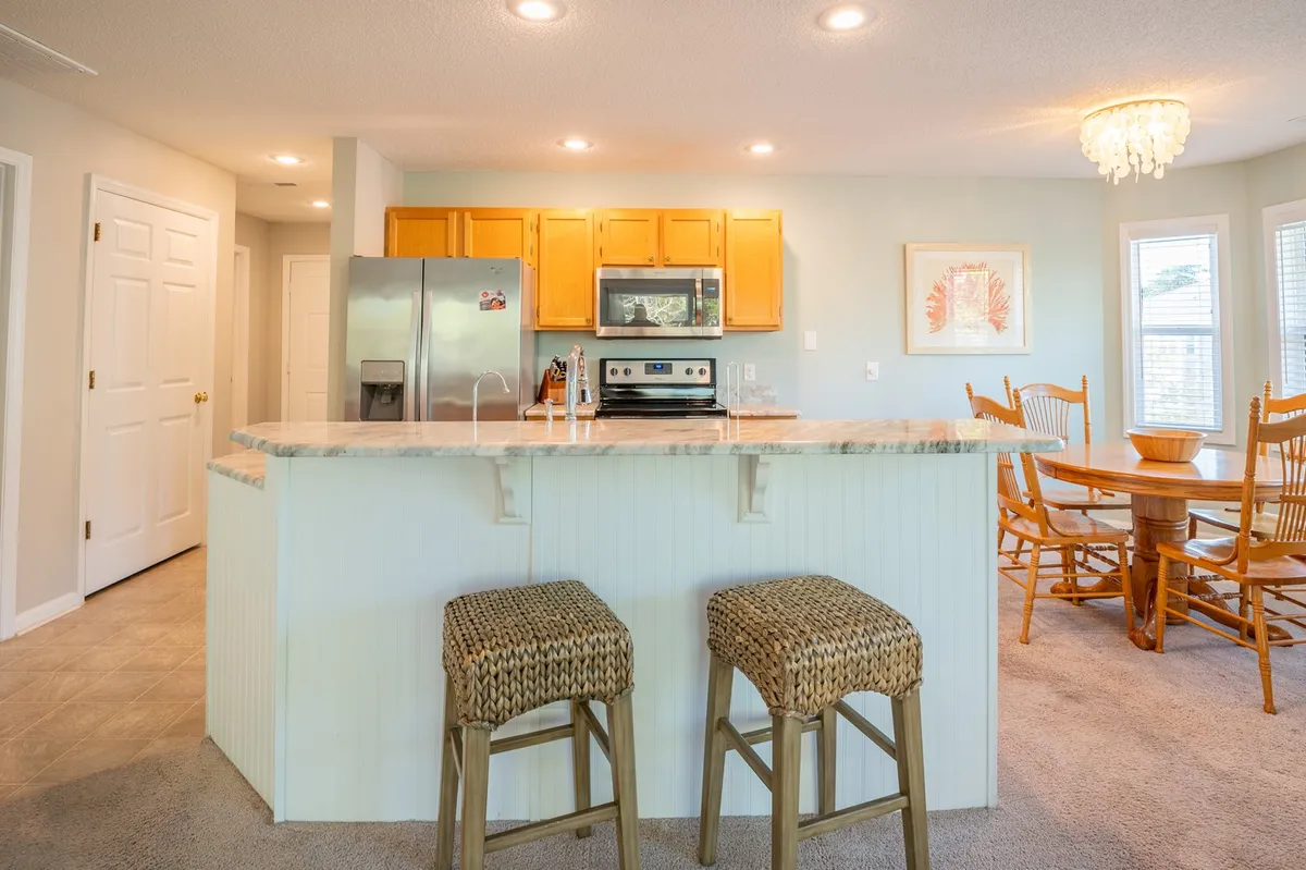 This image shows an open-concept kitchen and dining area. The kitchen island, stools, and adjacent dining table for four are all clearly visible, creating a seamless flow between the prep and dining zones. The refrigerator and oven are part of the scene, reinforcing the space's functionality and readiness for gatherings.