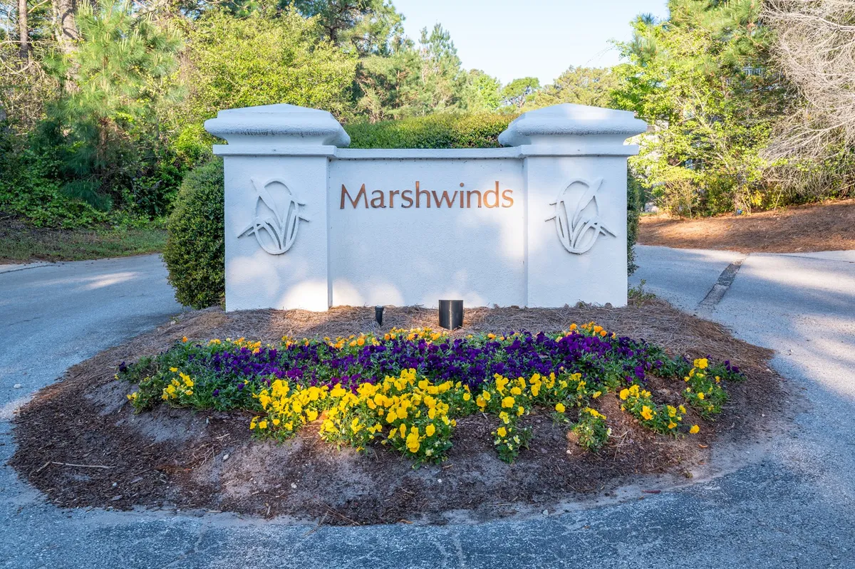 This image highlights the entrance sign to the community, surrounded by vibrant flower beds and manicured landscaping. Residents or visitors can be seen walking and exploring the area, with seasonal flowers providing a colorful, lively touch.