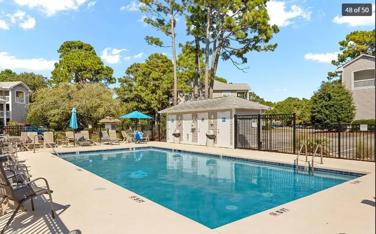 This image showcases the community swimming pool, complete with lounge chairs, umbrellas, and lush surrounding trees. The inviting pool area is set up for relaxation and socializing, capturing the leisurely atmosphere of resort-style amenities.