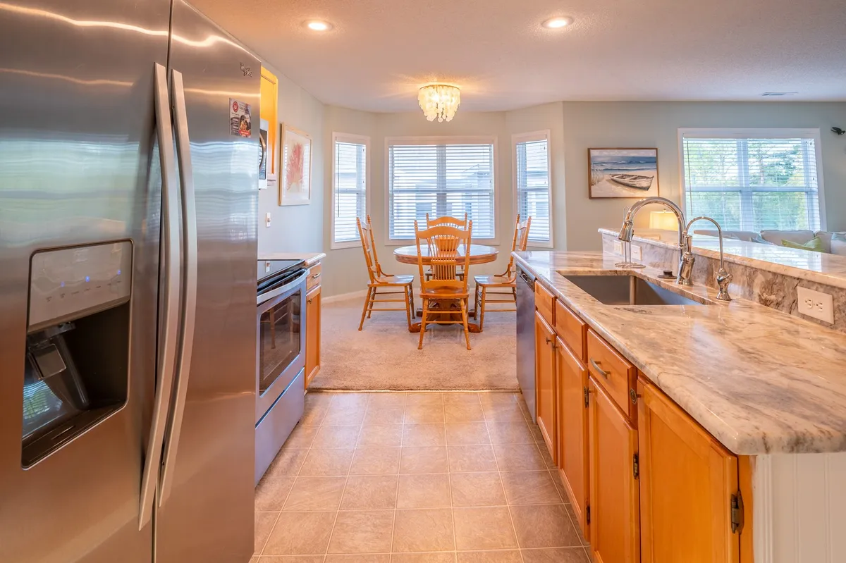 This image presents a welcoming interior view featuring a stainless steel refrigerator, marble countertop, and a dining table with chairs underneath a chandelier. The space is set up for family meals, entertaining guests, or simple everyday moments, all in a warm and inviting atmosphere.