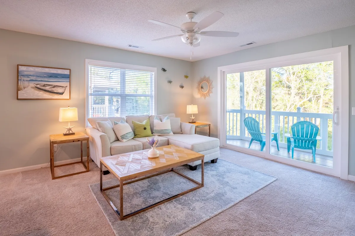 A cozy living room featuring a plush sectional sofa and a coffee table, bathed in sunlight from large windows. Through the windows, blue chairs are visible on the screened-in porch, offering a seamless transition between indoor and outdoor relaxation spaces.