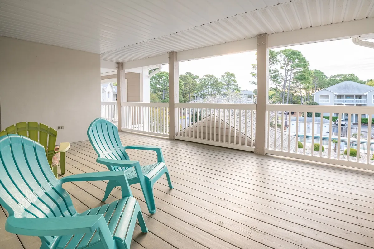 This image showcases a pair of turquoise Adirondack chairs set on a wooden deck, surrounded by lush trees. The view emphasizes a peaceful, natural atmosphere ideal for enjoying sunsets and the surrounding greenery.
