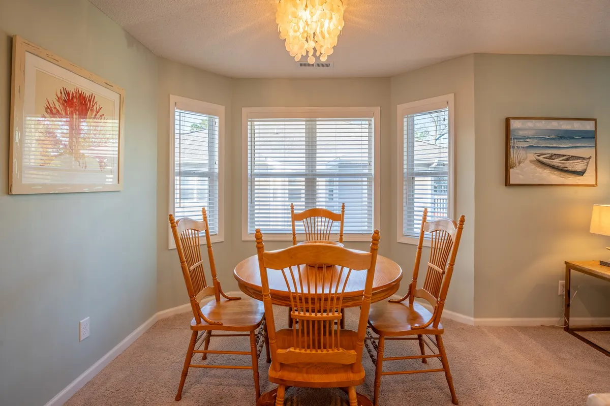 A dining area is bathed in natural light, featuring a cozy table set for four, an elegant chandelier, and tasteful wall art. The mood is warm and inviting, evoking a setting perfect for memorable meals, from quick breakfasts to romantic dinners.